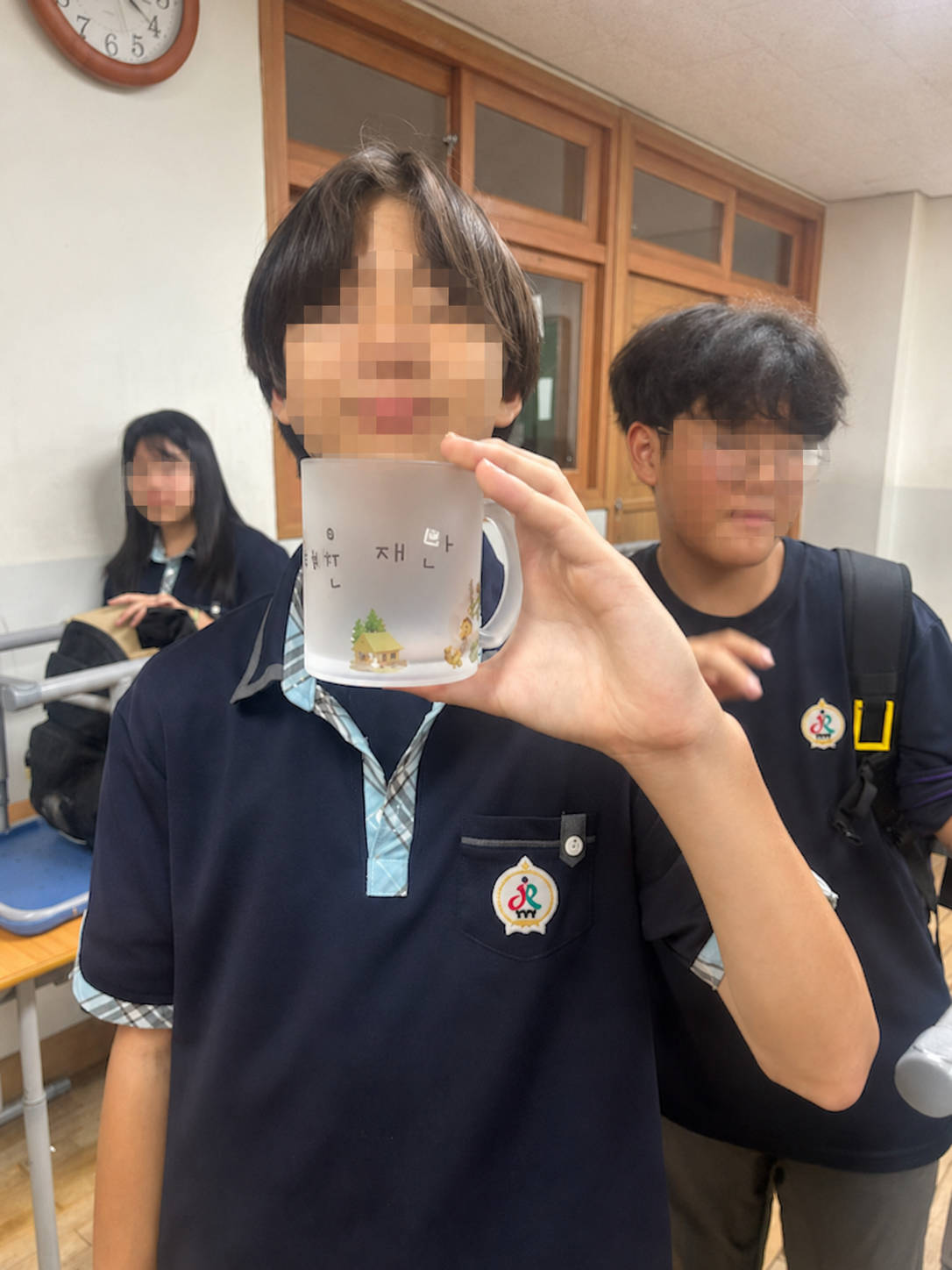 학생이 오두막 일러스트가 담긴 승화전사 머그컵을 들고 있는 모습